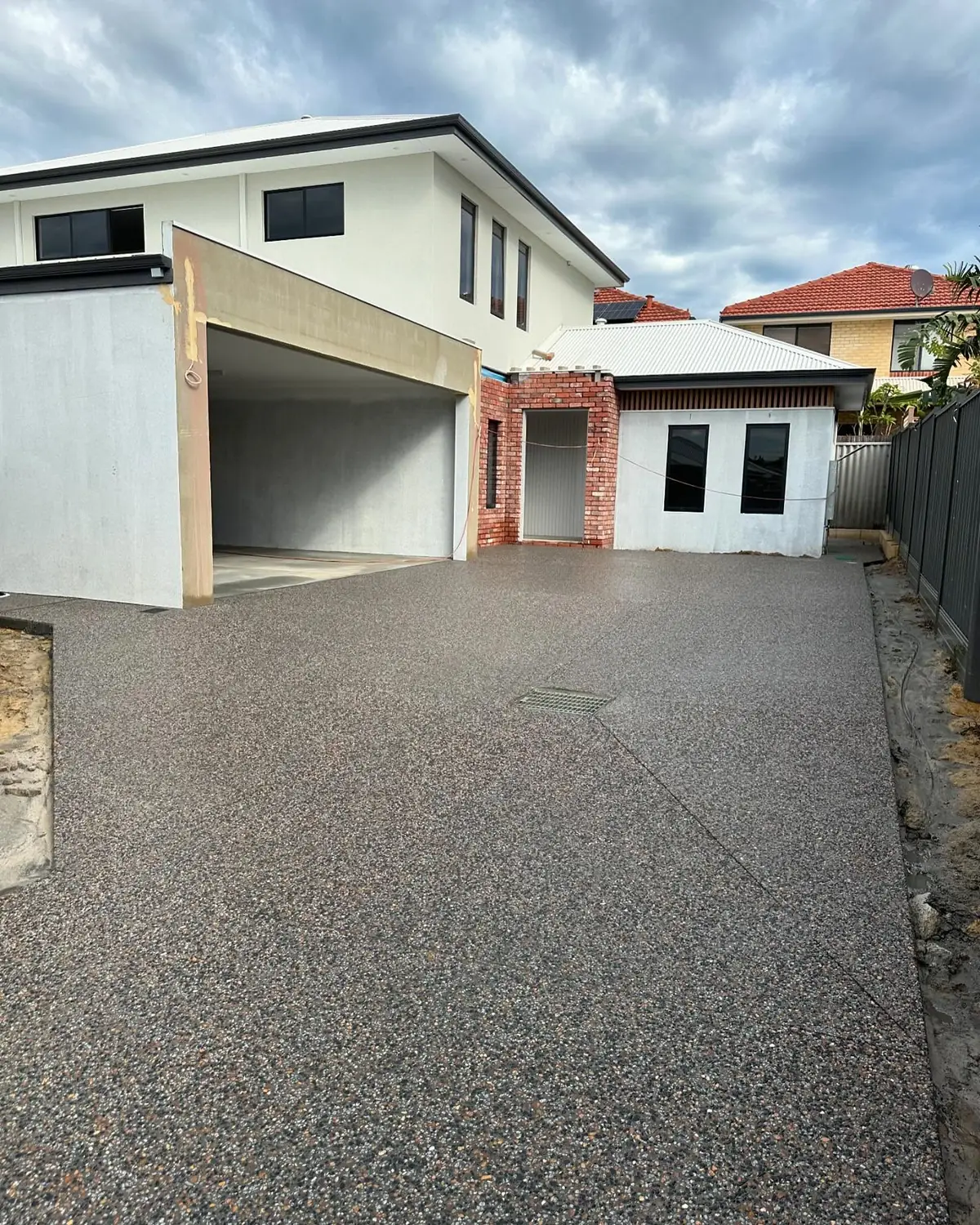 Dark exposed aggregate driveway in front of a two storey rendered house