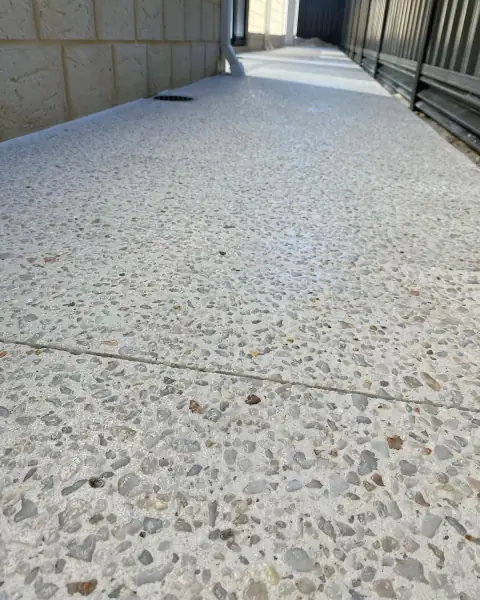 White exposed aggregate side path beside a limestone wall, with the joint cut through